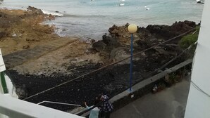 A coastal view with rocky terrain, a lamp post, and boats in the water.