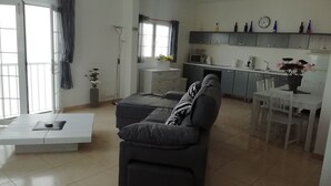 A modern living room with a sofa, a dining table, and a kitchen area with cabinets and a microwave.