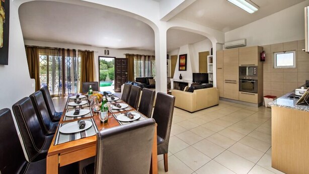 Un comedor amplio con techo alto y luz natural, una cocina con electrodomésticos modernos y una sala de estar acogedora con sofá y televisor.