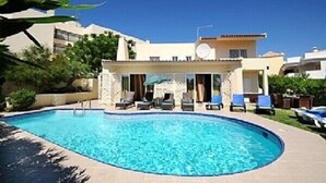 Piscina con sillones de descanso y una zona de estar cubierta, rodeada de edificios.