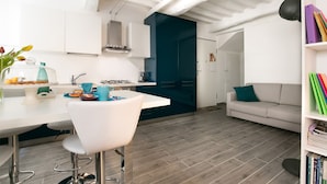 Una cocina moderna con armarios blancos, una isla azul oscuro y un comedor con mesa y sillas blancas.