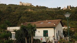 A white building with a tiled roof, green shutters, and a garden with palm trees. - Villa "LA GARITTA" Two steps from the magical village (Finale Ligure)