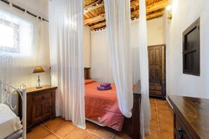 Une chambre à coucher avec un lit, une table de chevet, une armoire en bois et une fenêtre avec des rideaux.