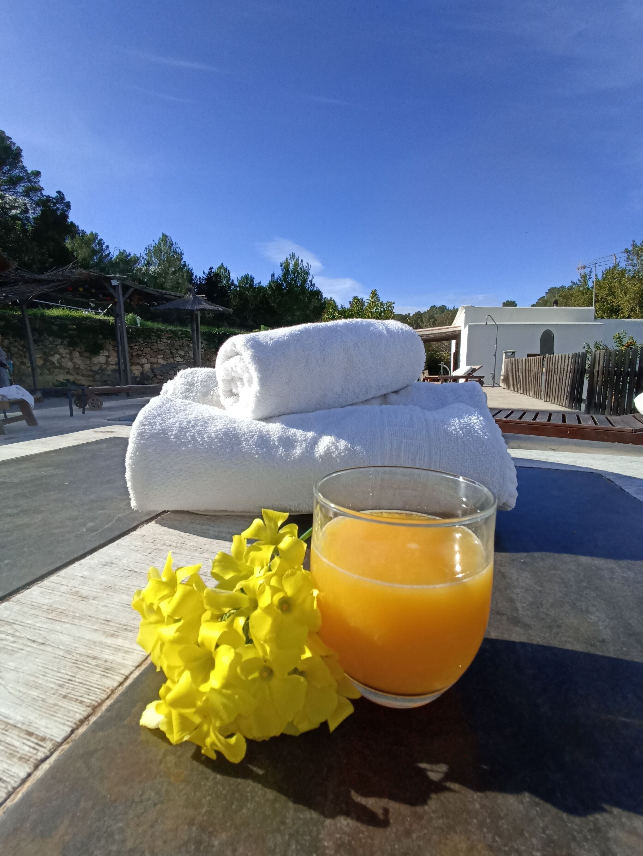 A table with towels and a glass of orange juice, set outdoors with a clear sky.