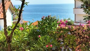 Een balkon met uitzicht op zee, omgeven door kleurrijke bloemen en een geel zonnescherm.