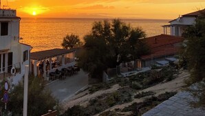 Een kustgezicht met een zonsondergang, een restaurant met terras en een gebouw met een rood dak.
