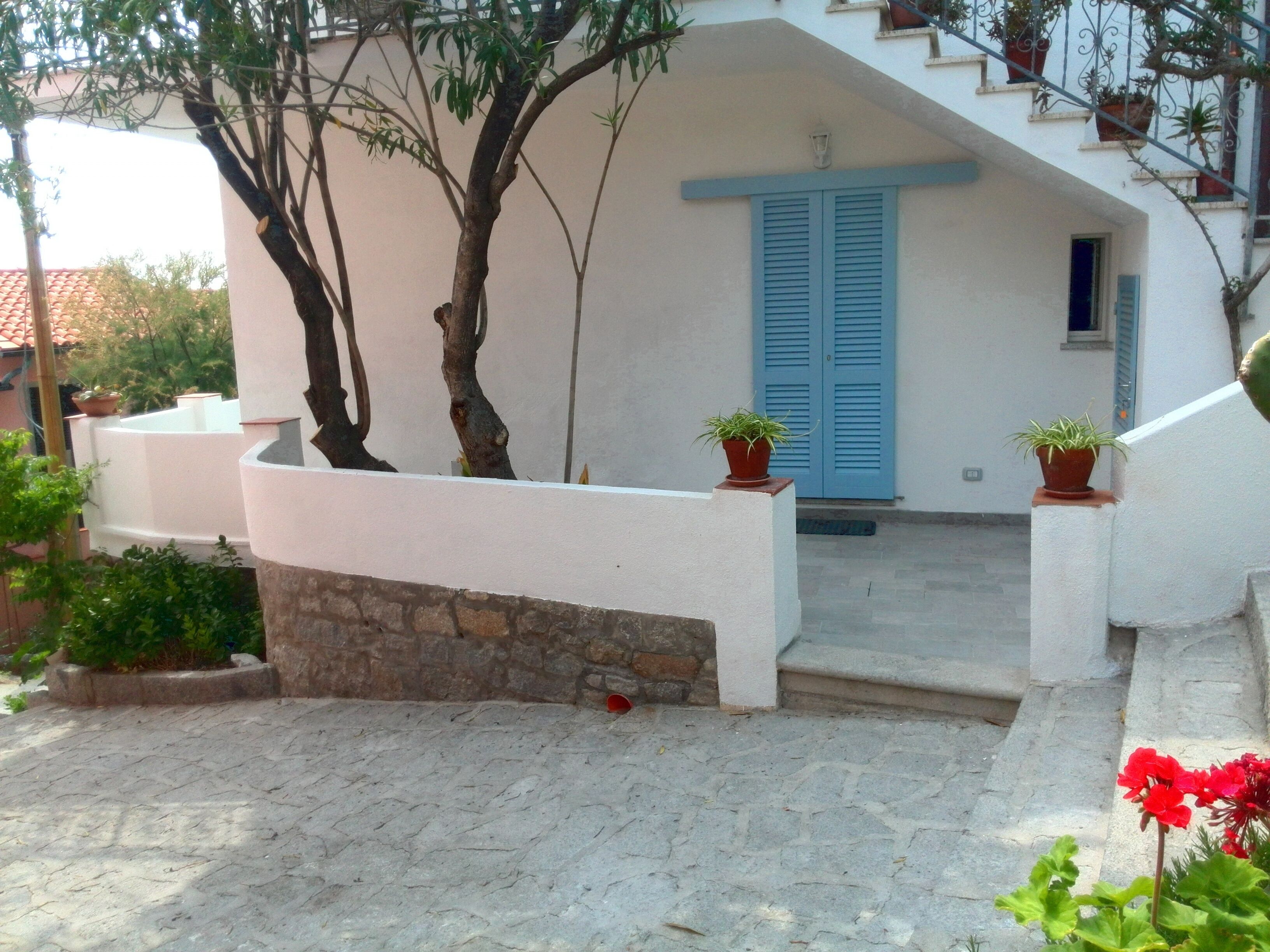 A white building with blue shutters, a stone wall, and potted plants.