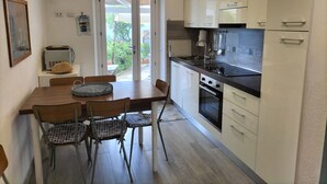 Een compacte keuken met witte kastjes, een zwart aanrecht en een eethoek met een houten tafel en stoelen met een patroon.
