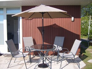 A patio with a round table and four chairs, an umbrella, and a door leading to a room.