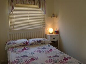A bedroom with a bed, a bedside table with a lamp, and a window with blinds.