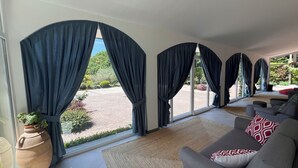 Ein geräumiges Wohnzimmer mit großen Fenstern, einem grauen Sofa und einer Topfpflanze.