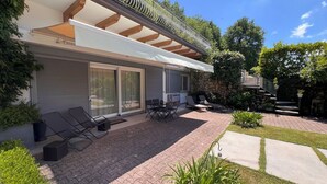 Ein modernes Haus mit Terrasse, Gartenmöbeln, einer Steinmauer und einem gepflegten Garten.