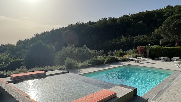 Ein Schwimmbecken unter einem sonnendurchfluteten Himmel, umgeben von einer gefliesten Terrasse und Liegestühlen.