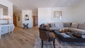 A modern living room with a sofa, a coffee table, and a chair. There is a dining area with a table and chairs. The room has a wooden floor and white walls.