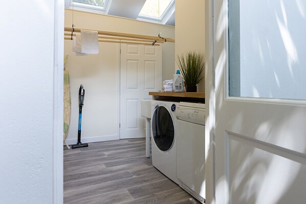 A laundry room with a washing machine, a drying rack, and a vacuum cleaner.