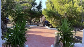 A paved pathway leading to a building with a stone wall and a blue car parked nearby. - Spacious sea view villa 3 minutes from the beach (Torre dei Corsari)