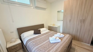 Ein ordentlich eingerichtetes Schlafzimmer mit Bett, Nachttisch, Schrank und einem Fenster mit Jalousien.