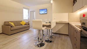 Eine moderne Küche mit Essbereich, einem Sofa mit gelben Kissen und einem an der Wand befestigten Fernseher.
