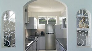 A compact kitchen with a stainless steel refrigerator, a gas stove, and white cabinetry.