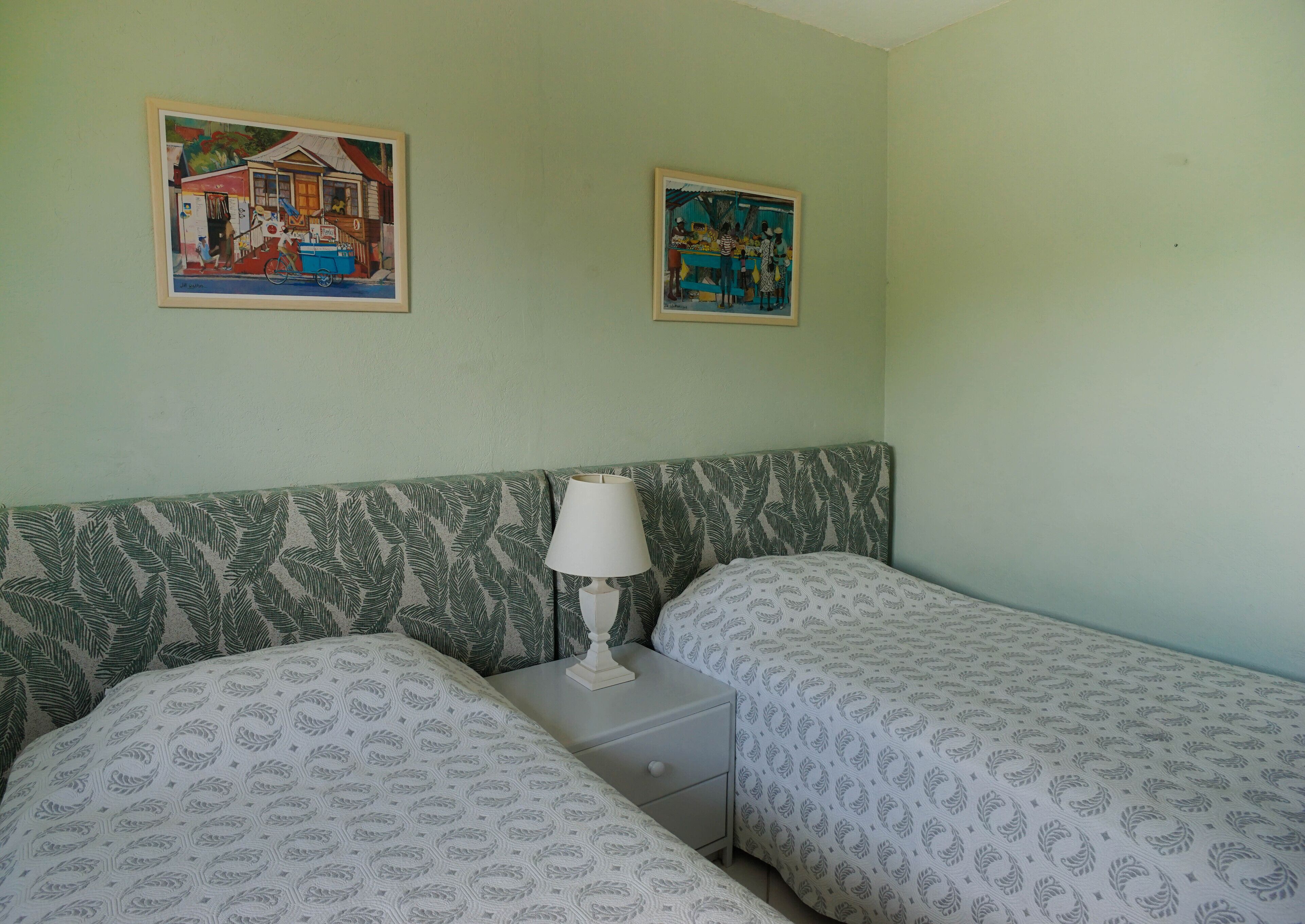 Une chambre avec deux lits, une table de chevet, une lampe et deux tableaux encadrés au mur.