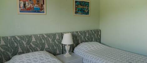 Une chambre avec deux lits, une table de chevet, une lampe et deux tableaux encadrés au mur.