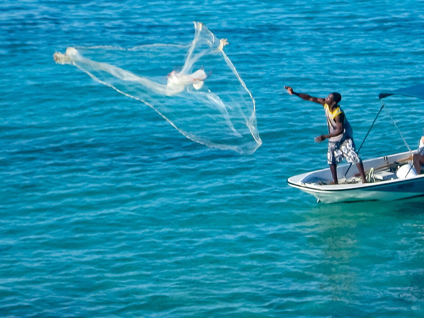 Une personne à bord d’un bateau lance un filet de pêche à l’eau.