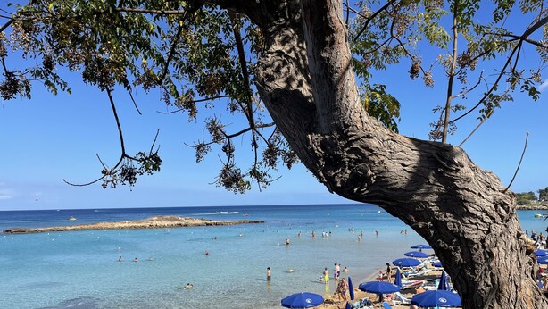 A beach with clear blue water, people swimming and sunbathing, and a rocky outcrop in the distance. - Beautiful 2 bedroom apartment with attractive views  (Oriklini)