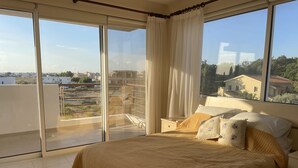 A bedroom with a large bed, a nightstand, and a view of the city through floor-to-ceiling windows. - Beautiful 2 bedroom apartment with attractive views  (Oriklini)