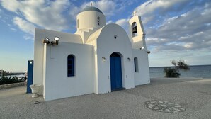 A white church with a blue door and bell tower, located near a body of water. - Beautiful 2 bedroom apartment with attractive views  (Oriklini)