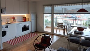 A modern kitchen with white cabinets, a built-in oven, and a dishwasher. There is a dining area with a table and chairs, and a balcony with a view of buildings. - STUNNING VIEWS NEAR THE BEACH. (Zarautz)
