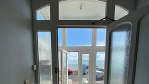 A hotel entrance with a glass door leading to a parking area and a view of the sea.
