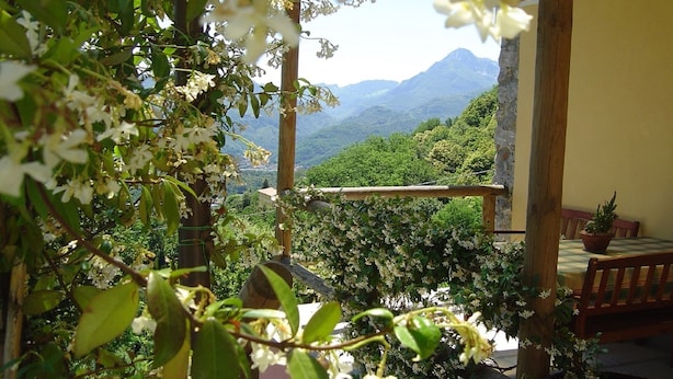 Un balcón con baranda de madera, una mesa con una silla y vistas a un paisaje montañoso.