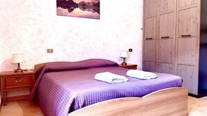 Un dormitorio con una cama, dos mesitas de noche, un armario de madera y un cuadro en la pared.