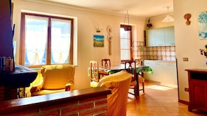 Un luminoso salón con sofá y sillones, un comedor con mesa y una cocina con armarios y fregadero.