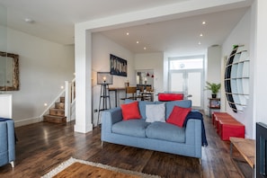 A modern living room with a grey sofa, wooden flooring, and a staircase leading to an upper level. - Stunning seaside with cinema room, sea views  - ideal for friends and families (Newquay)