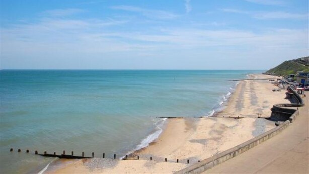 A beach with a concrete walkway, calm sea, and a clear sky.