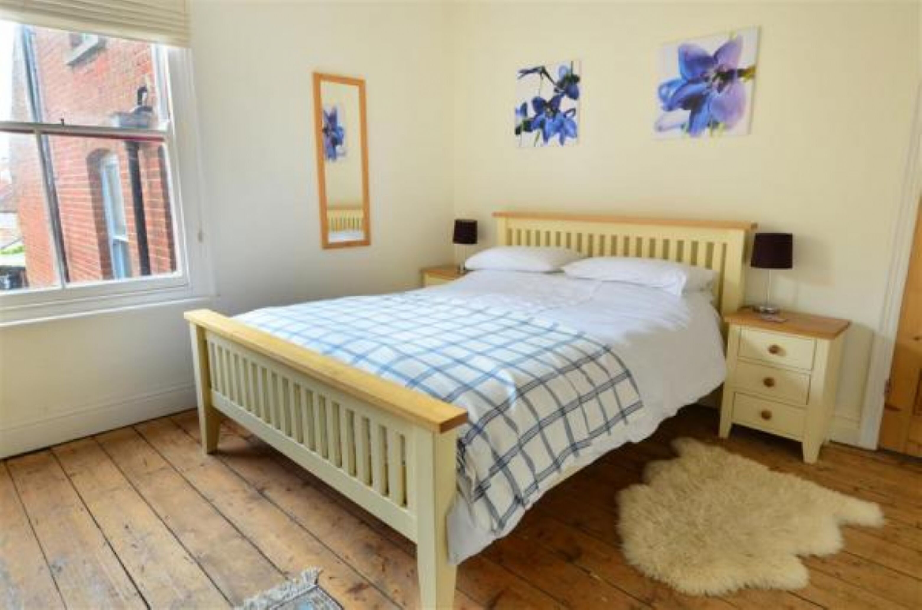 A bedroom with a wooden bed, a nightstand, a fluffy rug, and two wall-mounted flower paintings.