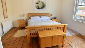 A bedroom with a wooden bed, bedside tables, a nightstand, a window with a view, and a painting on the wall.