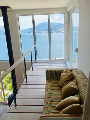 Enjoy the serene view of the water and distant landforms from this balcony, featuring a comfortable sofa and metal railing.
