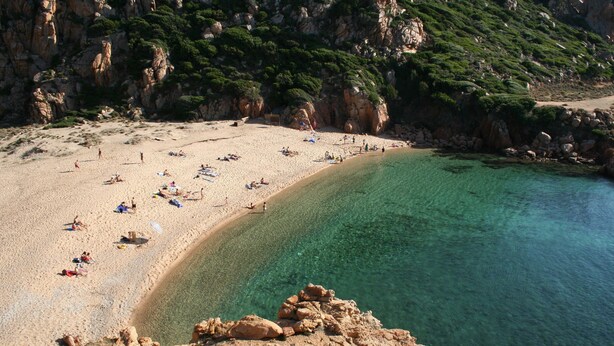 A beach with clear water, rocky cliffs, and people sunbathing.