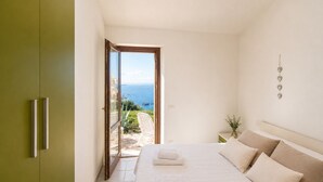 A bedroom with a bed, a green wardrobe, a view of the sea, and a wall decoration.