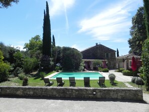 A stone house with a swimming pool, surrounded by lush greenery and a stone wall.