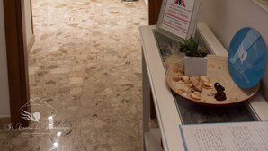 Um corredor com porta de madeira, espelho, placa proibindo fumar e uma bandeja com conchas e uma pequena planta.