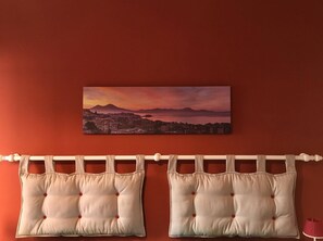 A room with a red wall, a cityscape painting, and two beige pillows with red buttons.