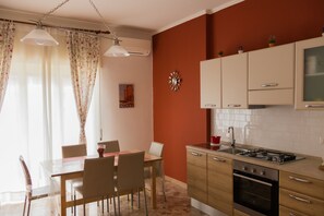 A kitchen with a gas stove, oven, and white cabinets. There is a dining table with chairs and a window with curtains.