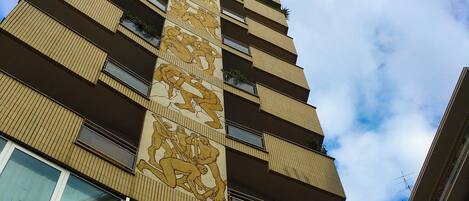 Um edifício alto com um design vertical marcante, apresentando um mural grande em uma das laterais e várias sacadas.