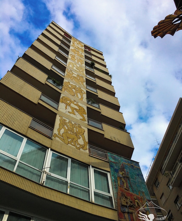 A tall building with a distinctive vertical design, featuring a large mural on one side and multiple balconies.
