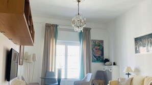 Olohuone, jossa on sohva, sohvapöytä, kattokruunu, televisio ja patsas.