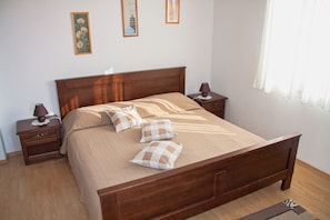 A neatly made bed with a wooden headboard, two bedside tables with lamps, and a window with sheer curtains.