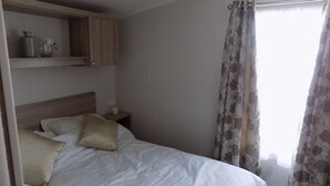 Ein Schlafzimmer mit einem Bett, einem Nachttisch, einem Regal mit Dekoration und einem Fenster mit Vorhängen.